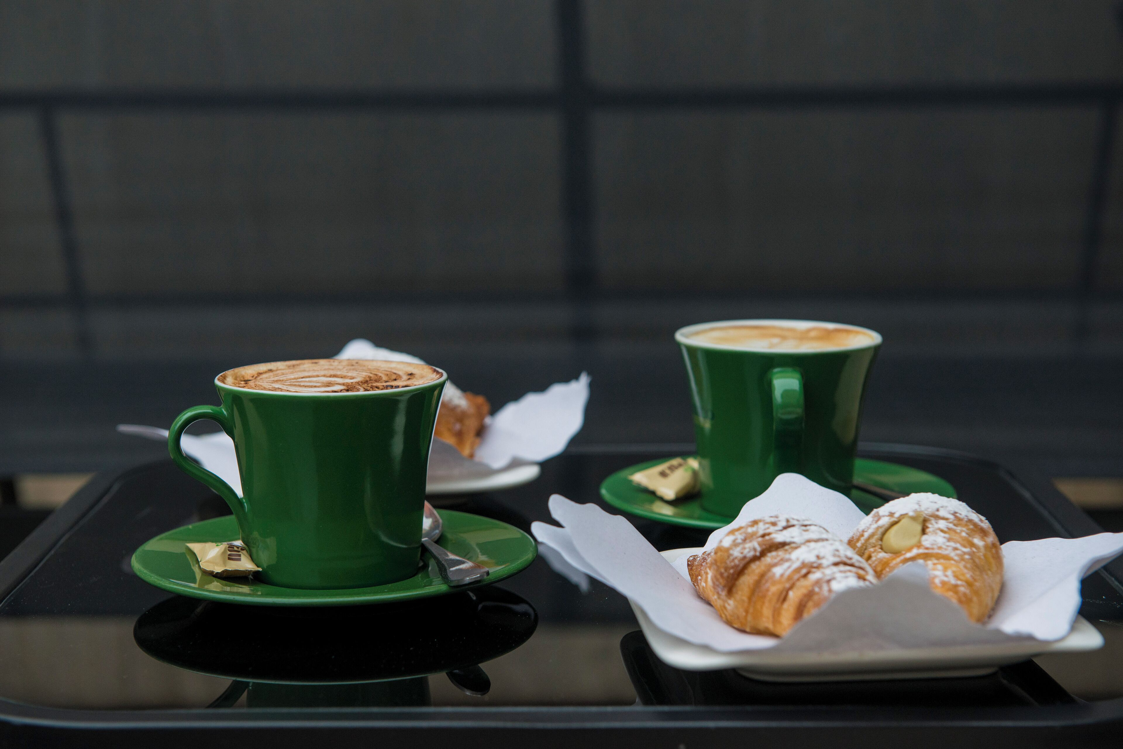 A table with two green cups of coffee and two pastries on white plates.