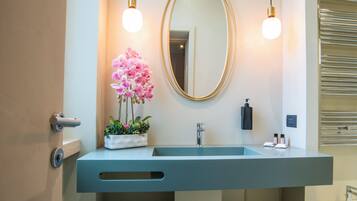 A modern bathroom with a large mirror, two pendant lights, a sink, and a potted orchid.