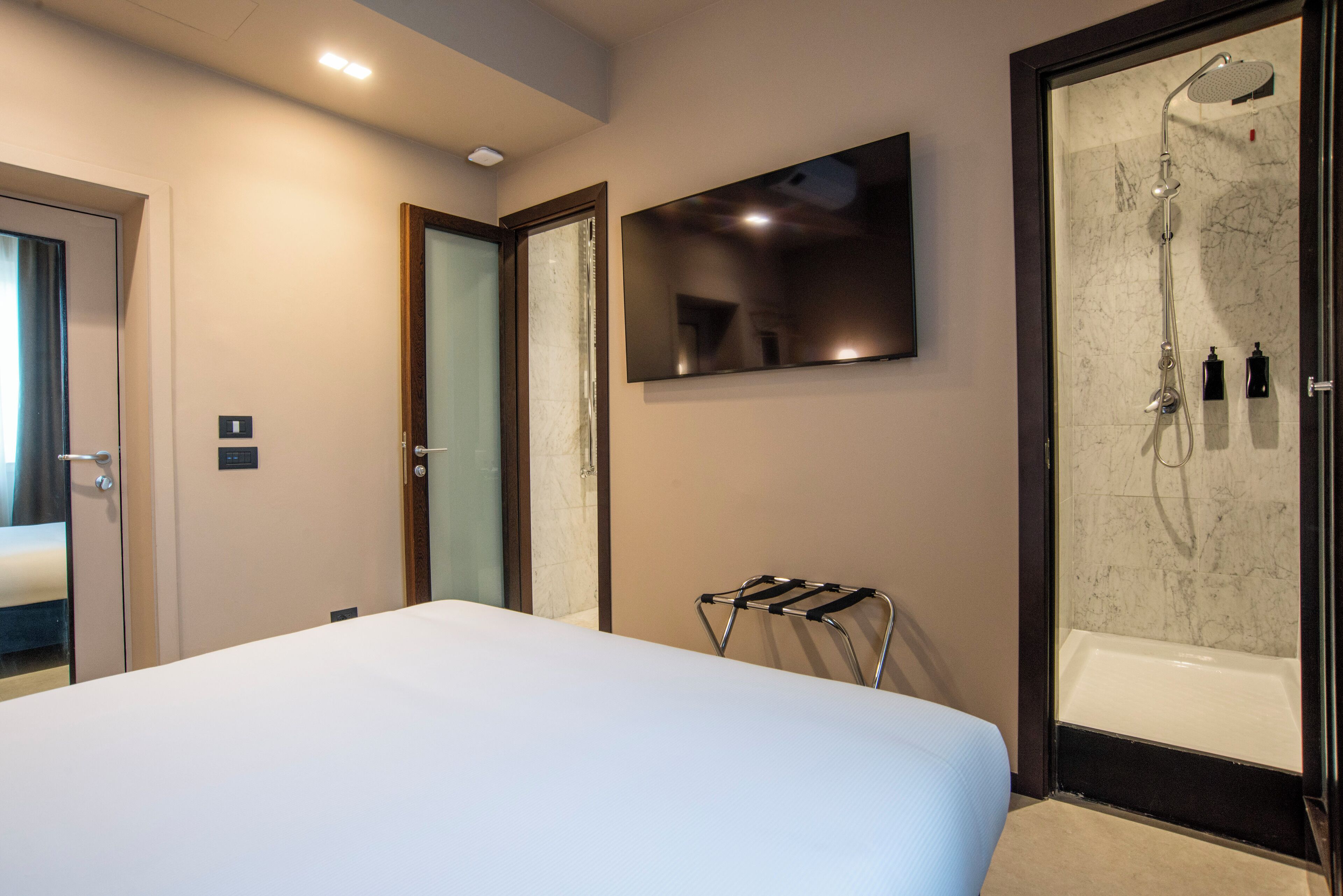 Ein Hotelzimmer mit einem großen Bett, einer Dusche mit Glastür, einem an der Wand montierten Fernseher und einem Handtuchhalter.