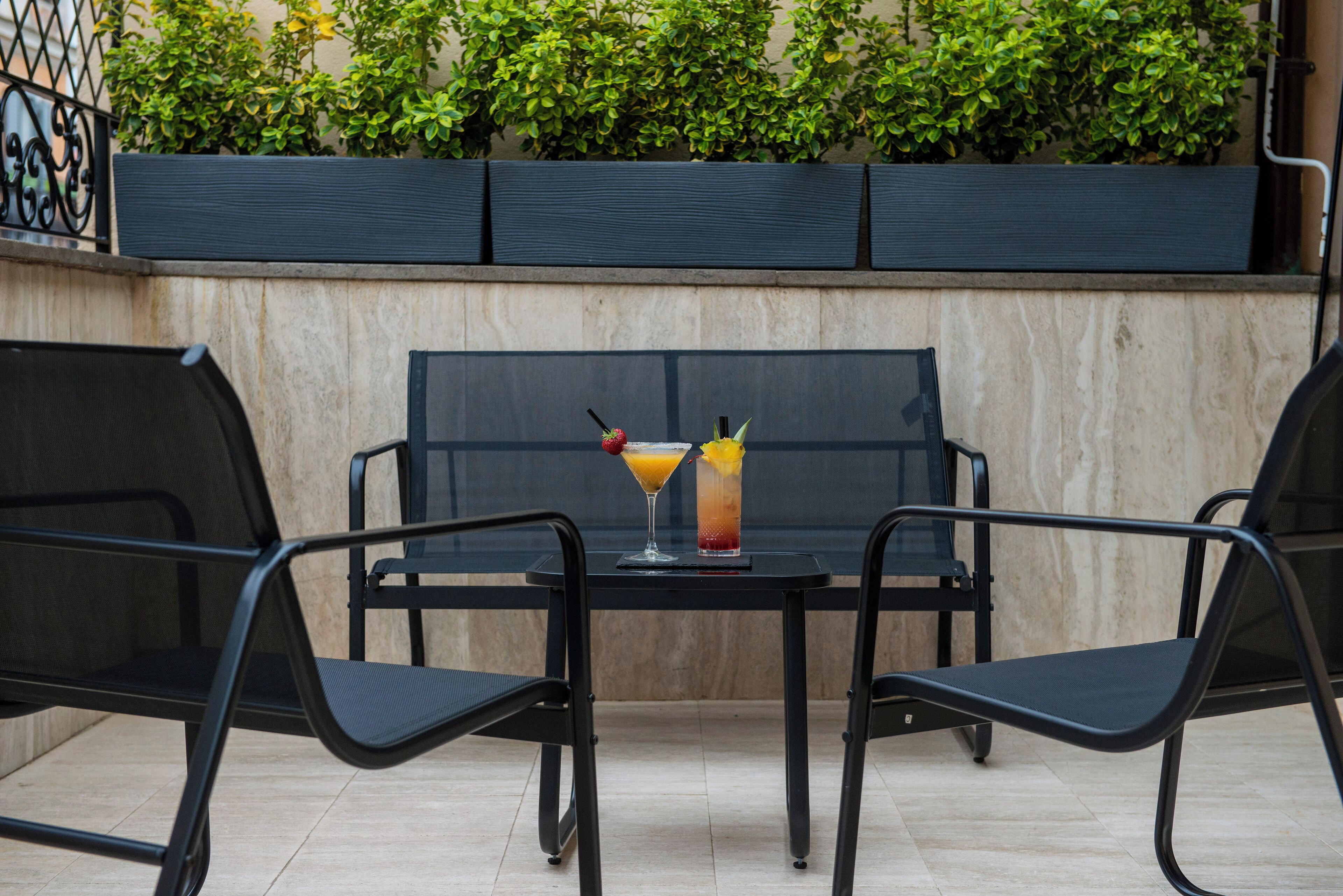 Een tafel met twee stoelen, een glas ijsthee en een cocktail met rietje en kers.