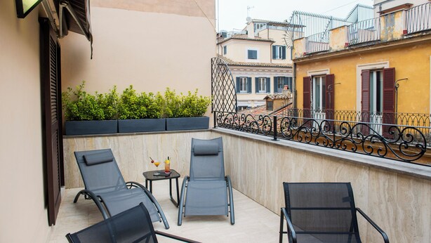 A balcony with four lounge chairs, a small table with a drink, and a decorative metal railing. - Bocca di Leone Luxury Suite (Rome)