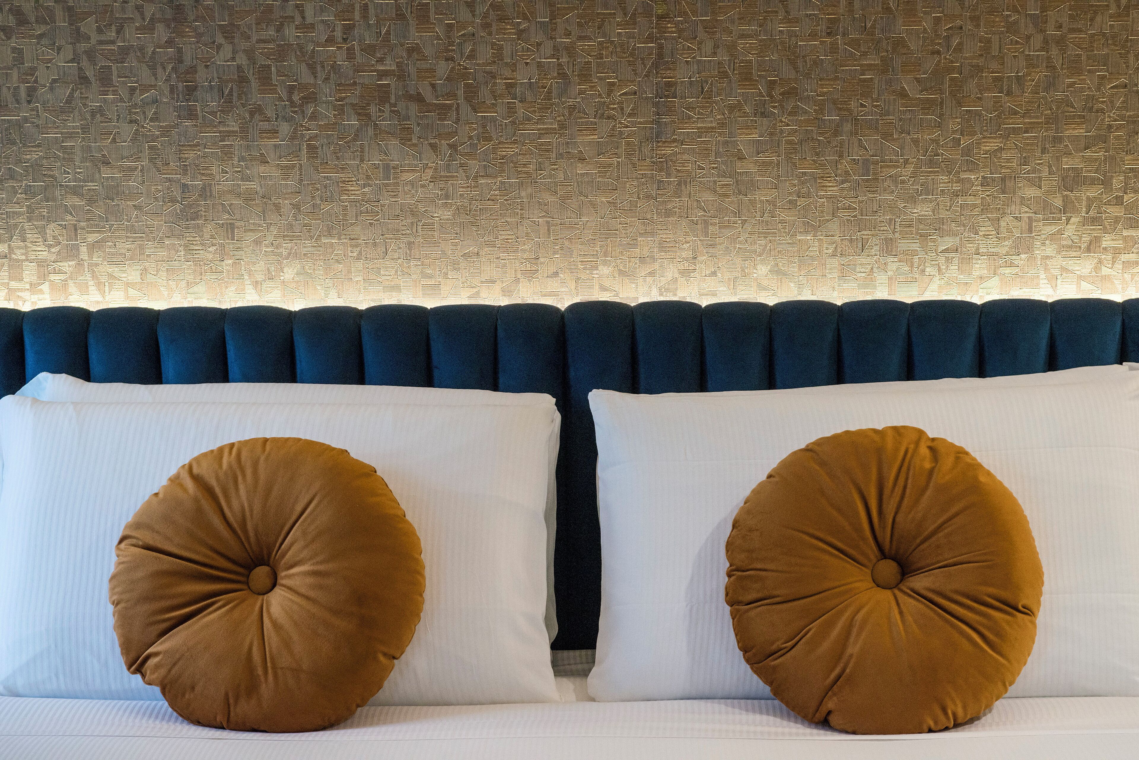 A bed with a blue headboard, two white pillows, and two brown accent pillows.