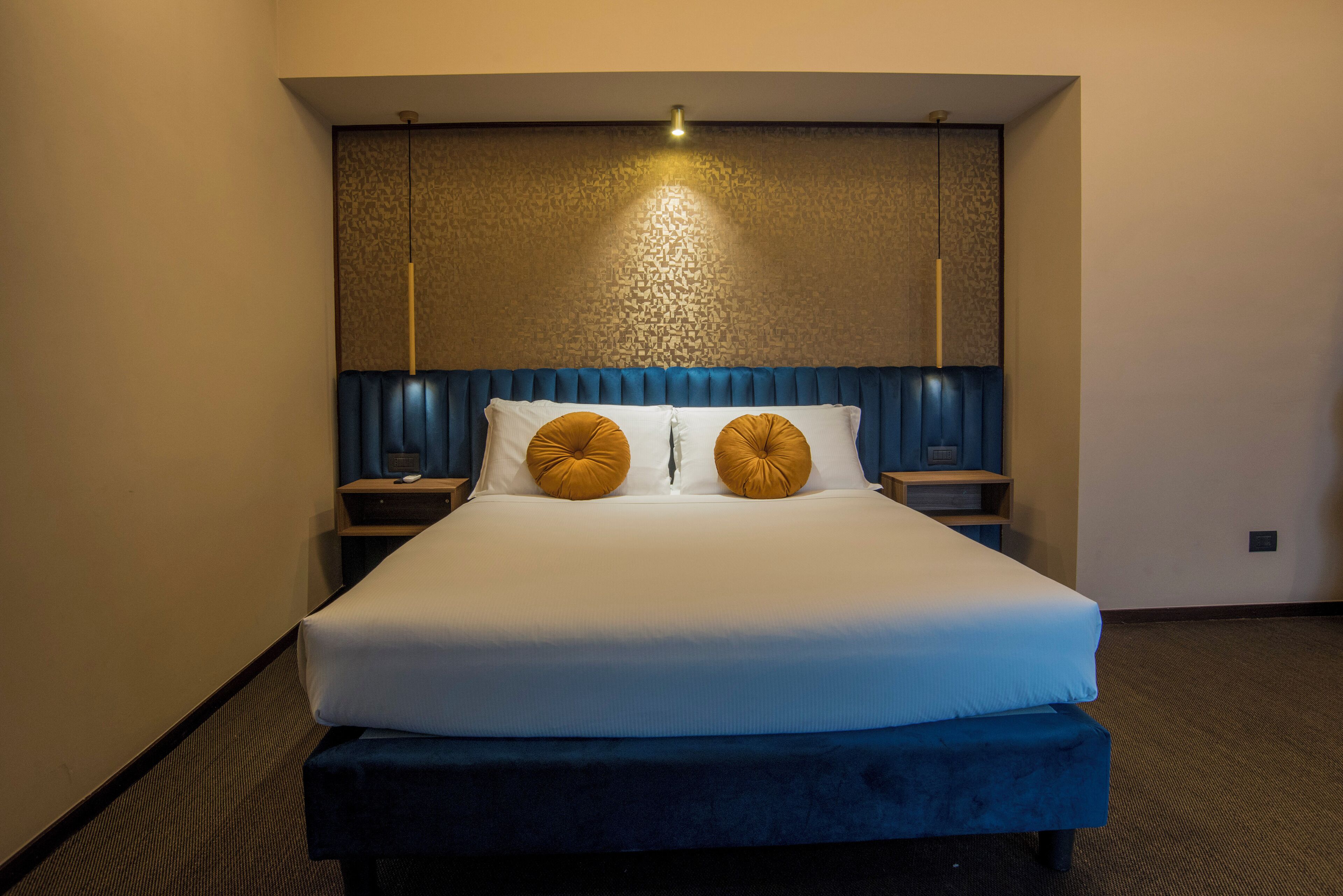 A hotel room with a large bed, two bedside tables, a headboard with a light fixture, and a carpeted floor.