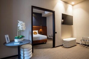 A modern hotel room with a bed, a small table with a plant, a seating area, and a TV mounted on the wall. - Bocca di Leone Luxury Suite (Rome)