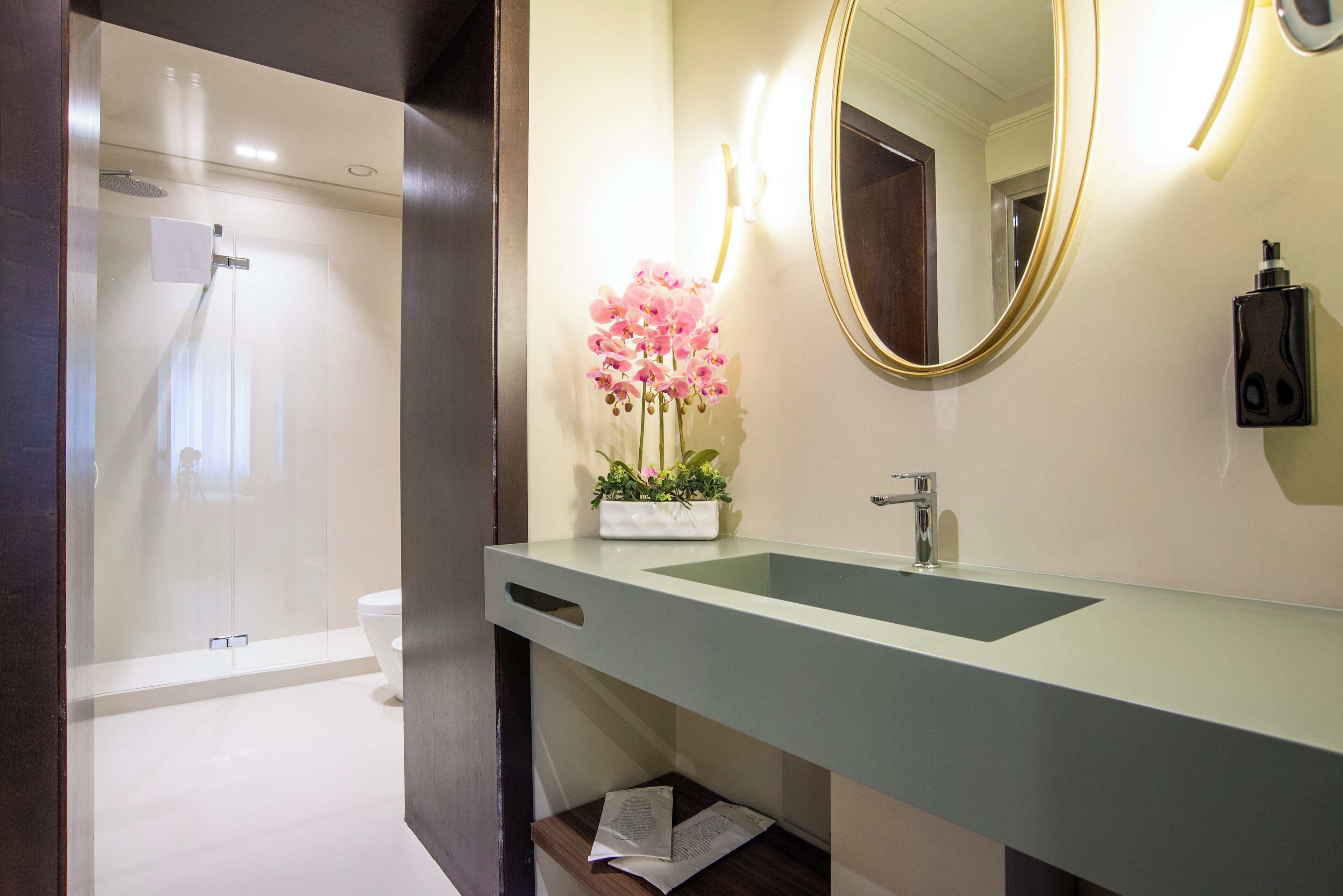 Une salle de bain moderne avec une douche à parois de verre, un lavabo avec un miroir et un vase rempli de fleurs roses.