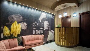 A reception area with a large poster, a pink sofa, a marble coffee table, and a wooden reception desk. - Bocca di Leone Luxury Suite (Rome)