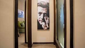 A hallway with a large portrait on the wall, a green sofa in the background, and a glass door with a monogram. - Bocca di Leone Luxury Suite (Rome)