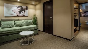 A hotel room with a green sofa, a small round table, and a large framed picture on the wall. - Bocca di Leone Luxury Suite (Rome)
