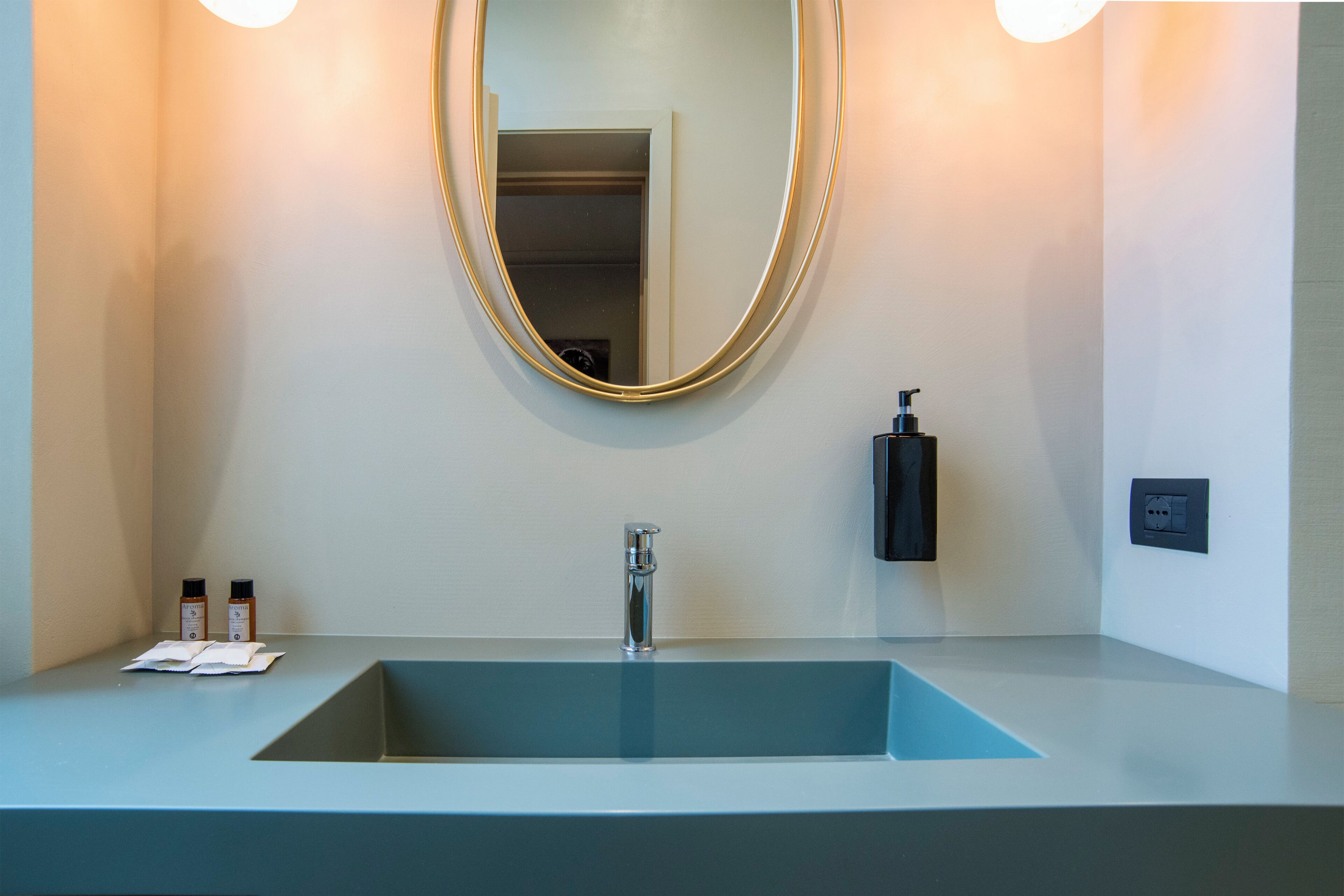 Une salle de bain moderne avec un lavabo rectangulaire, un grand miroir et deux bouteilles de shampoing posées sur le comptoir.