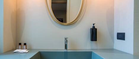Une salle de bain moderne avec un lavabo rectangulaire, un grand miroir et deux bouteilles de shampoing posées sur le comptoir.