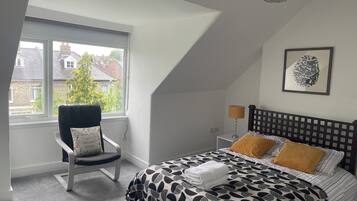Un dormitorio con cama, una silla, una lámpara y una ventana con vista a casas.