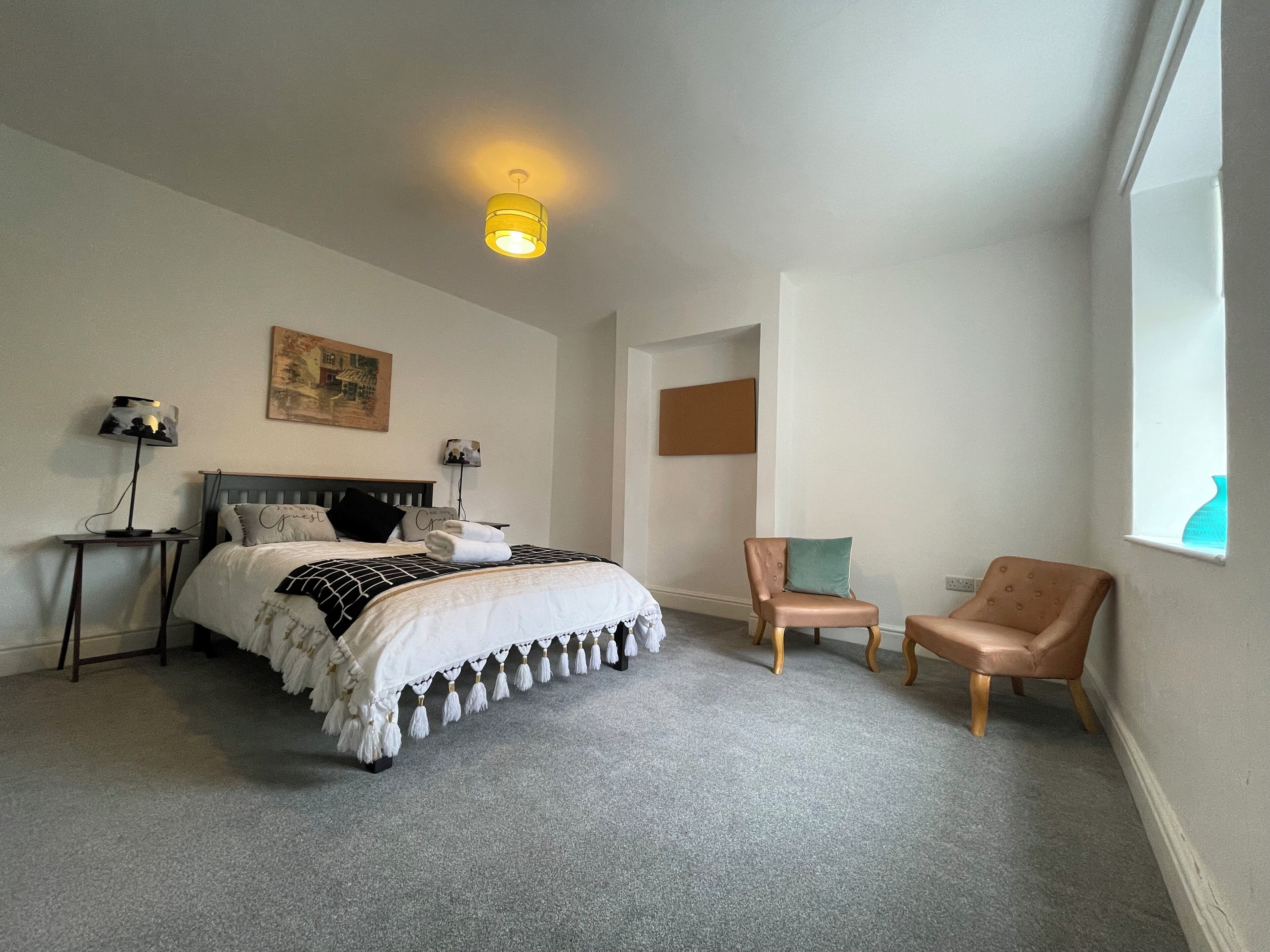A bedroom with a bed, two chairs, a nightstand, a lamp, and a painting on the wall.