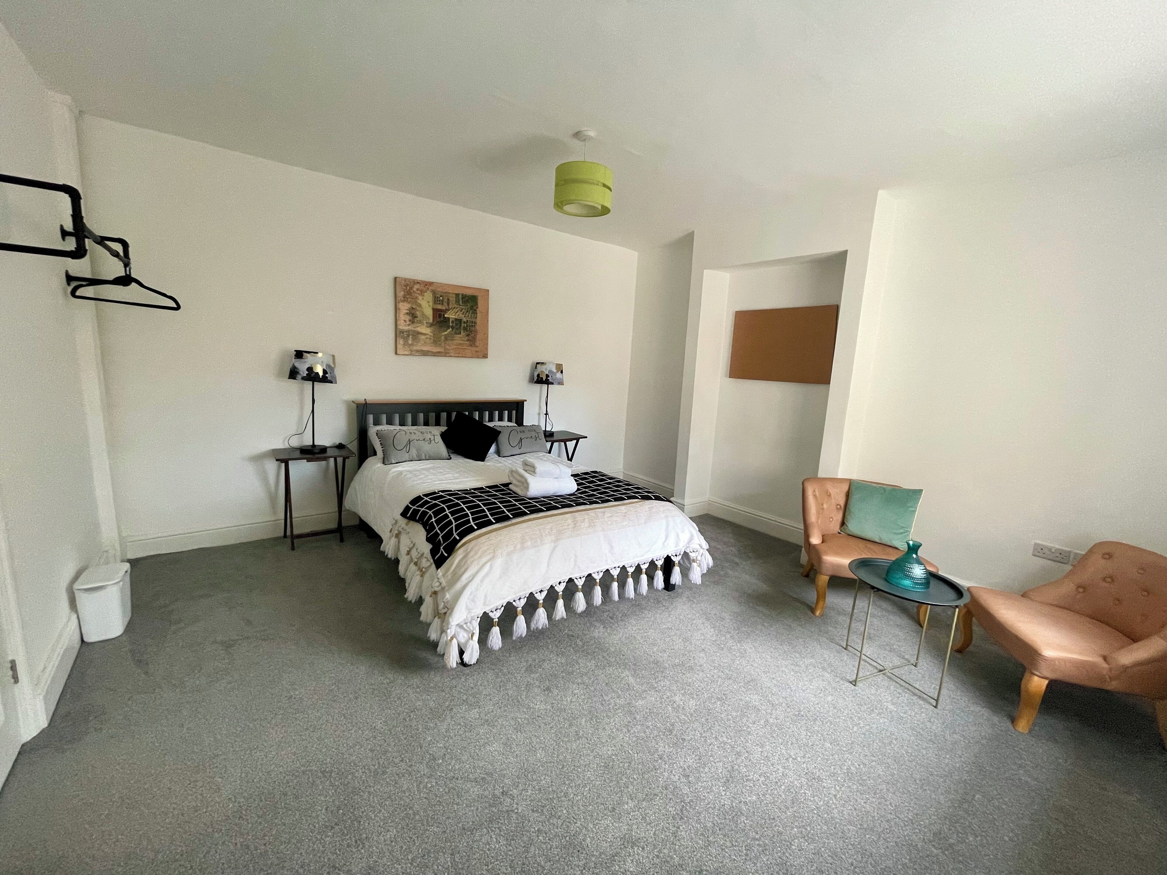 A bedroom with a bed, bedside tables, a chair, a hanging light fixture, and a picture on the wall.