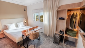 A hotel room with a bed, desk, chair, and a walk-in closet with hanging clothes.