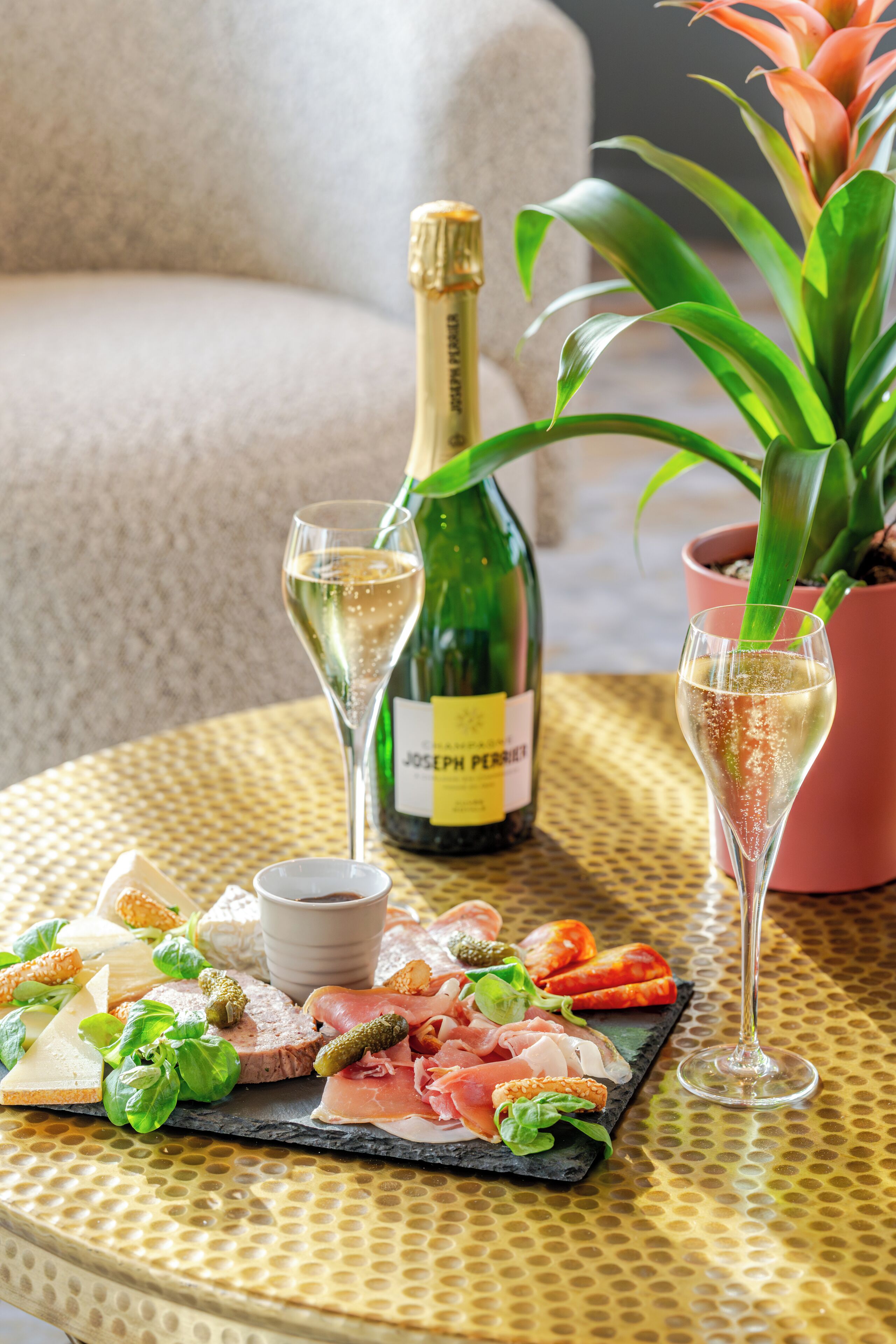 A table with a bottle of champagne, a glass of champagne, a bottle of wine, a glass of wine, a plate of food, and a potted plant.