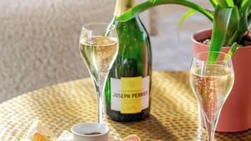 A table with a bottle of champagne, a glass of champagne, a bottle of wine, a glass of wine, a plate of food, and a potted plant.