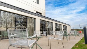 An outdoor seating area with metal chairs and tables, a building with large windows, and a clear sky.