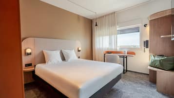 Une chambre d’hôtel avec un grand lit, une petite table, une chaise et une vue sur la ville par la fenêtre.