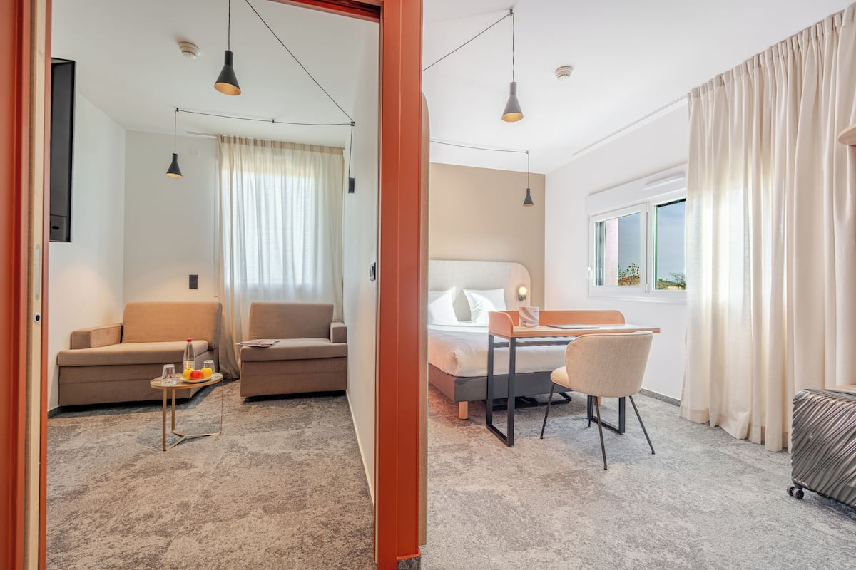 A hotel room with a bed, a desk, a chair, a sofa, and a small table with a bottle and glasses.