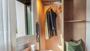 A compact room with a desk, laptop, camera, and a seating area with a chair and cushion.
