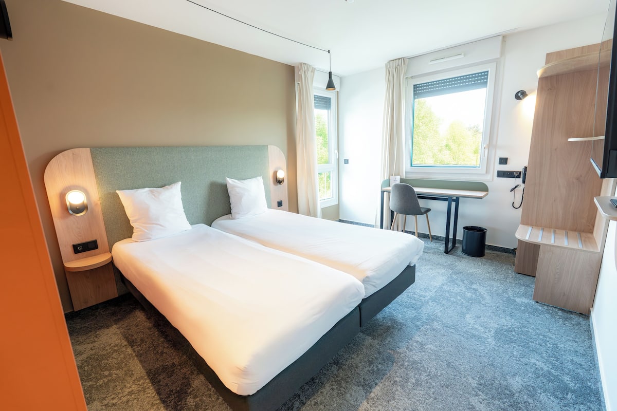 A hotel room with two beds, a desk, a chair, and a TV.