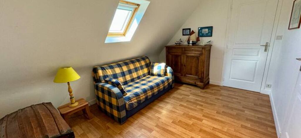 A room with a wooden floor, a checkered sofa, a small table with a lamp, a cabinet, and a door.