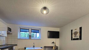 A compact kitchen with a wooden island, a dining table, and a TV mounted on the wall.