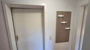 A hallway with a closed door, a wall-mounted light switch, and a wooden panel with a vertical design.