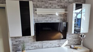 Una sala moderna con un televisor de pantalla plana montado en una pared de ladrillo, un mueble blanco debajo y un armario blanco con puertas abiertas.