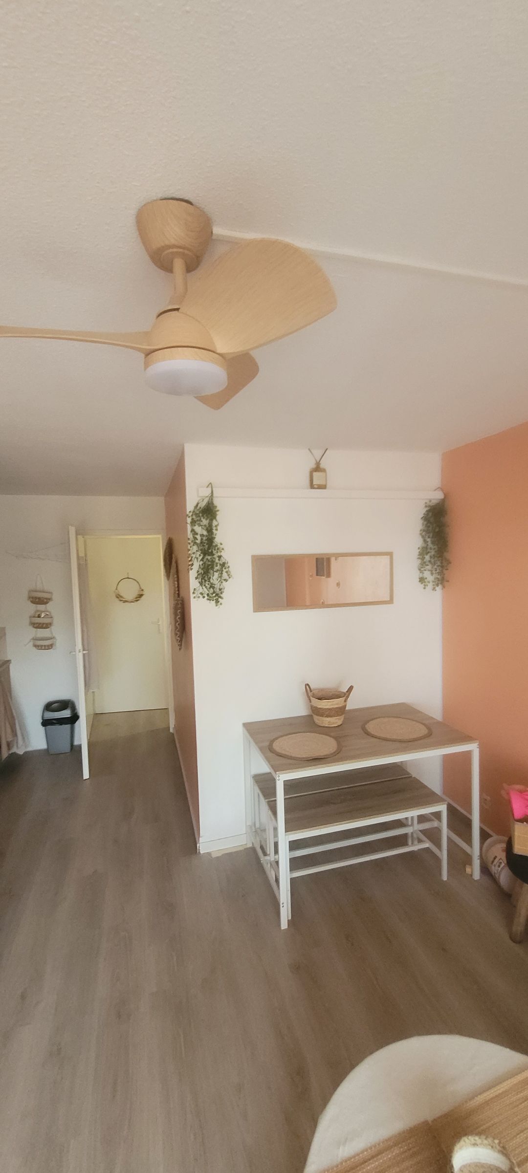 Una habitación con ventilador de techo, una mesa con espejo y una puerta que da a otra habitación.