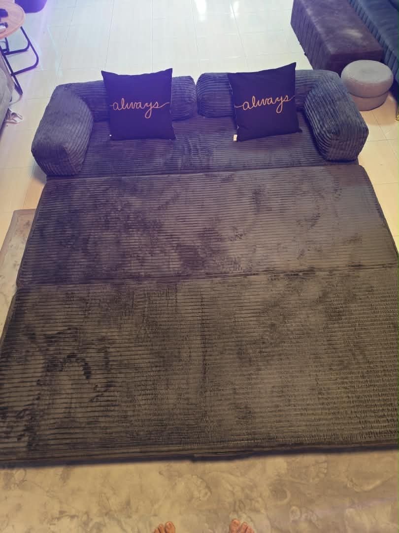 A dark-colored sofa with two pillows, one with the word 'always' on it.