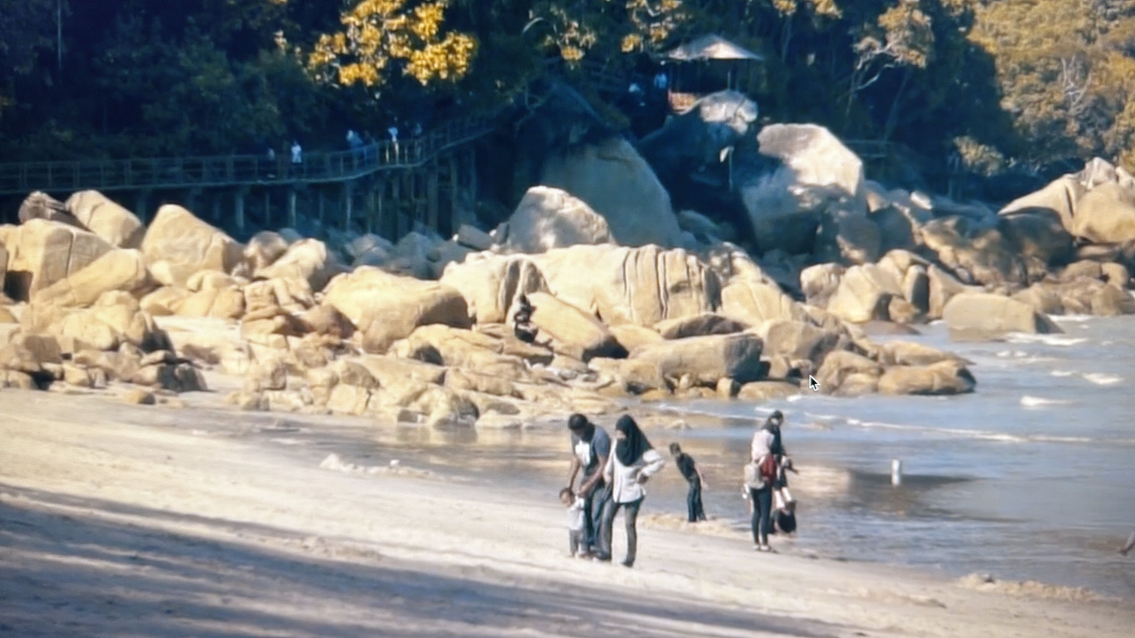 A beach with large rocks and a wooden walkway.