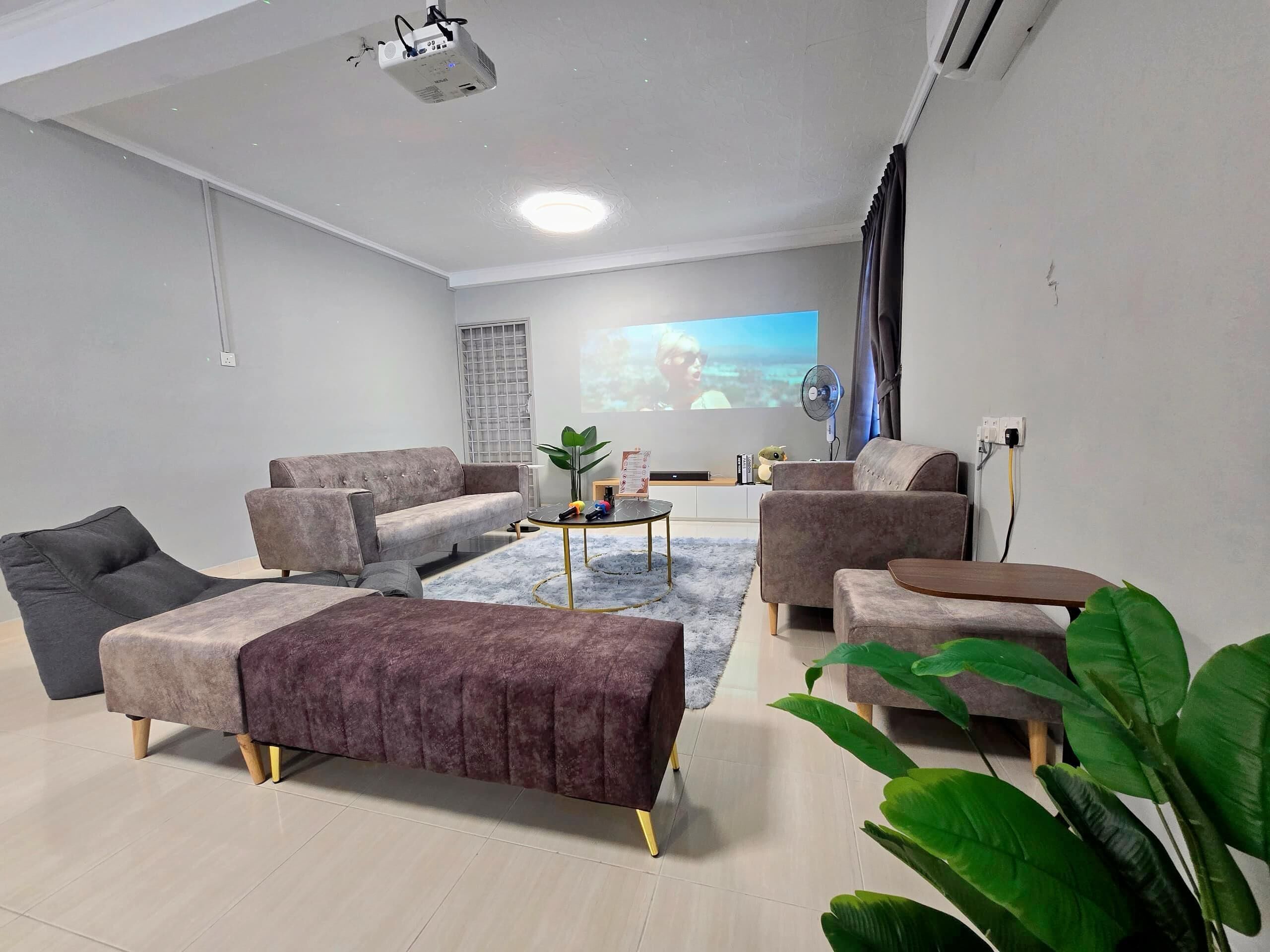 A modern living room with a large flat-screen TV, comfortable seating, and a ceiling projector.
