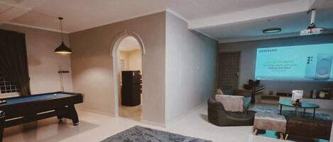 A modern living room with a pool table, comfortable seating, and a projection screen displaying a Samsung advertisement.