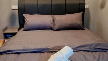 Una cama bien hecha con un cabecero oscuro, dos mesitas de noche y un cuadro colgado en la pared.