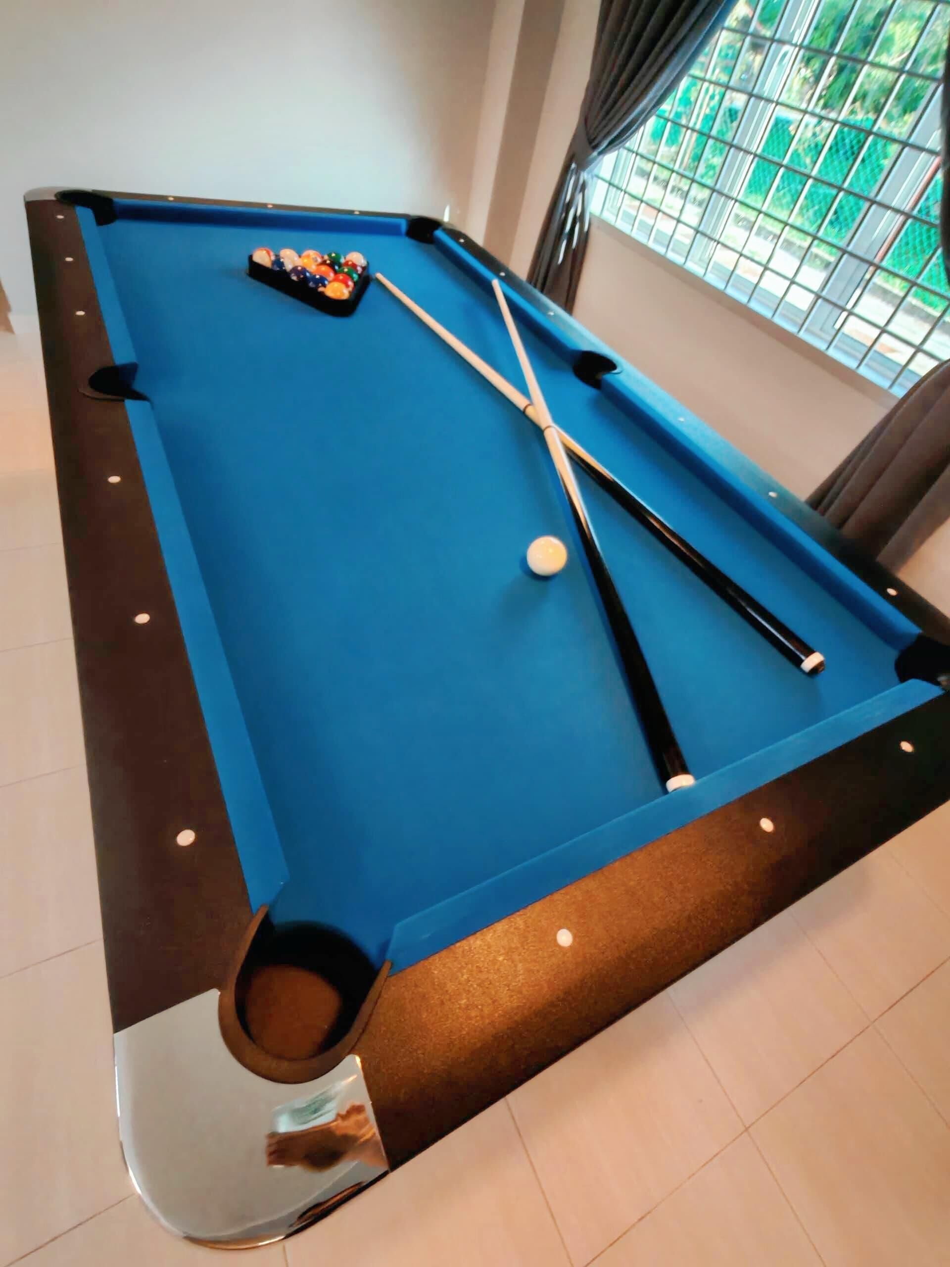 Une table de billard avec des billes et des queues, une fenêtre donnant sur un paysage verdoyant et un sol carrelé.