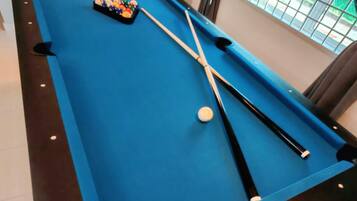 Une table de billard avec des billes et des queues, une fenêtre donnant sur un paysage verdoyant et un sol carrelé.