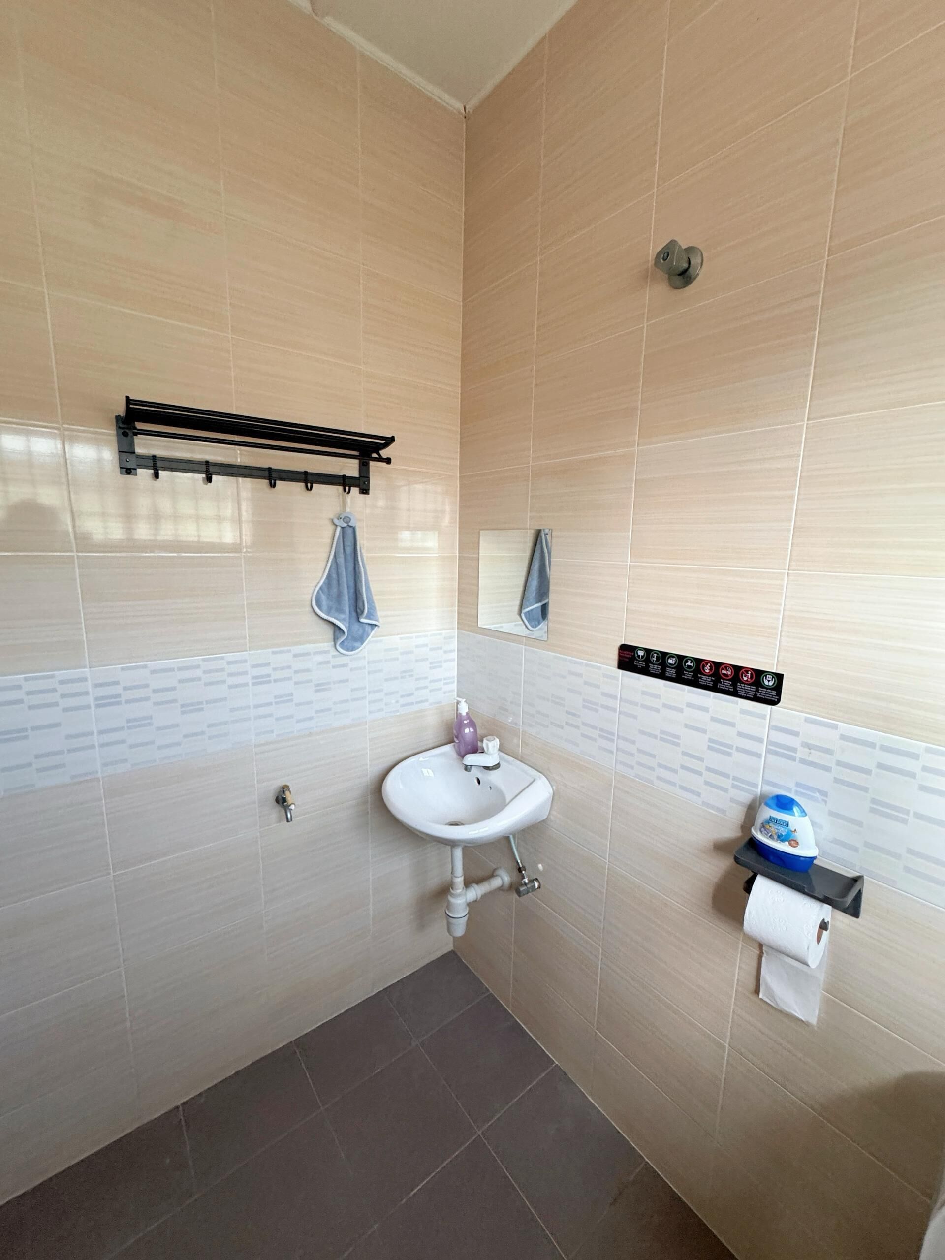 A bathroom with beige tiled walls, a white sink with a soap dispenser, a towel rack, a toilet paper holder, and a hand dryer.