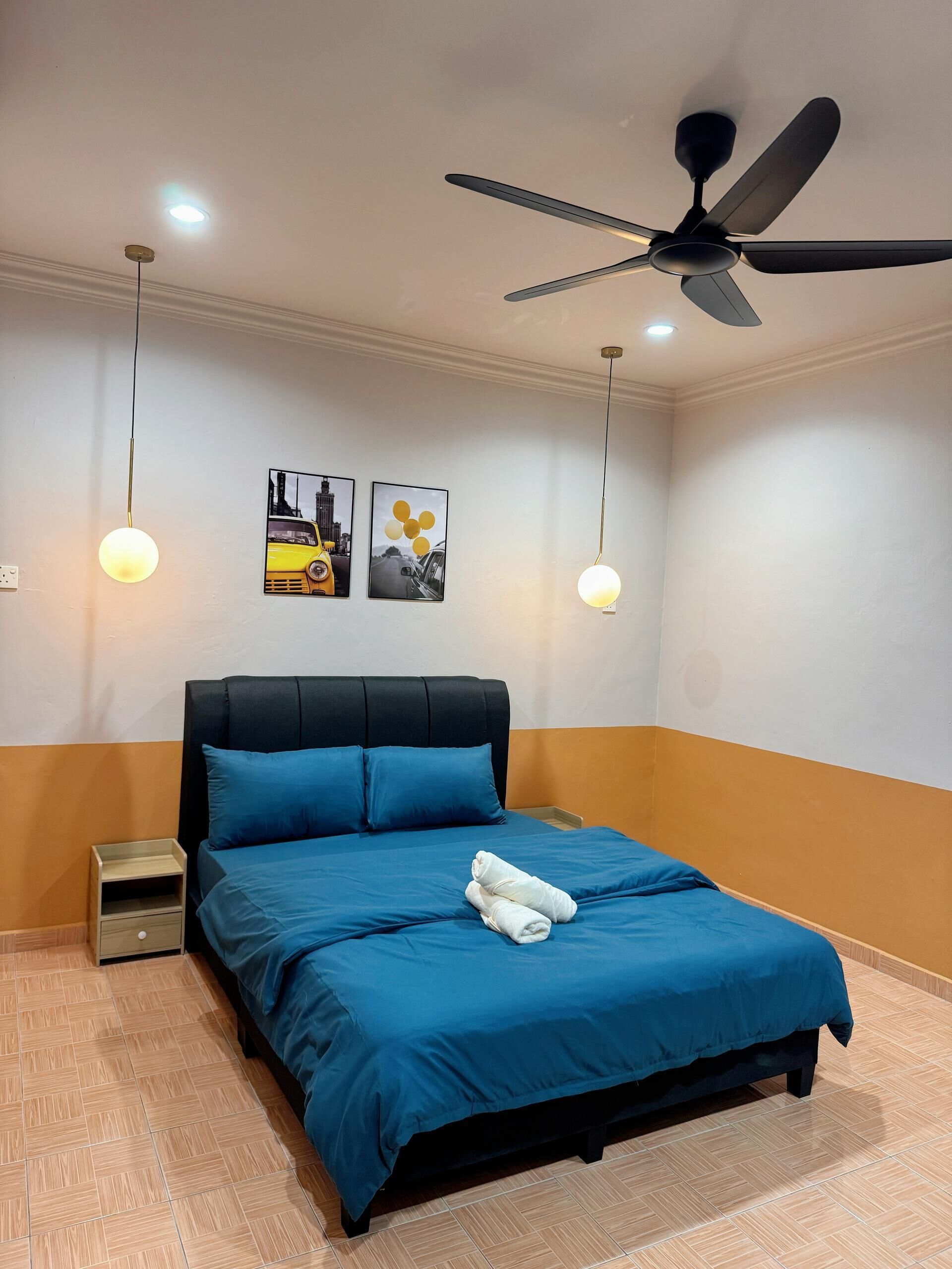 A neatly made bed with blue bedding, a ceiling fan, and two wall-mounted light fixtures.