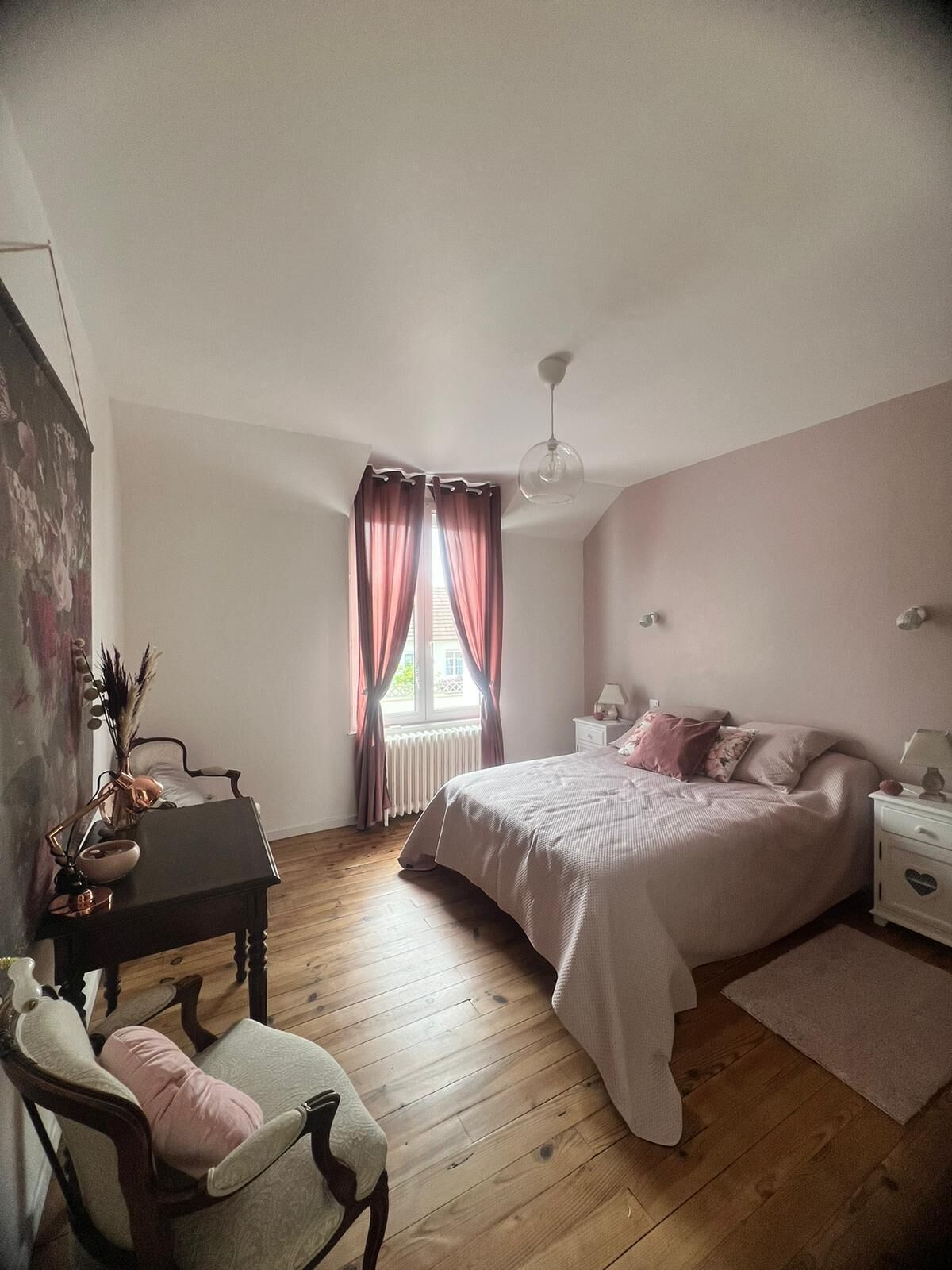 Un dormitorio con cama, una silla, un escritorio y una ventana con cortinas.