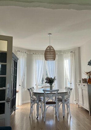 Uma sala de jantar com uma mesa redonda, cadeiras brancas e um lustre.