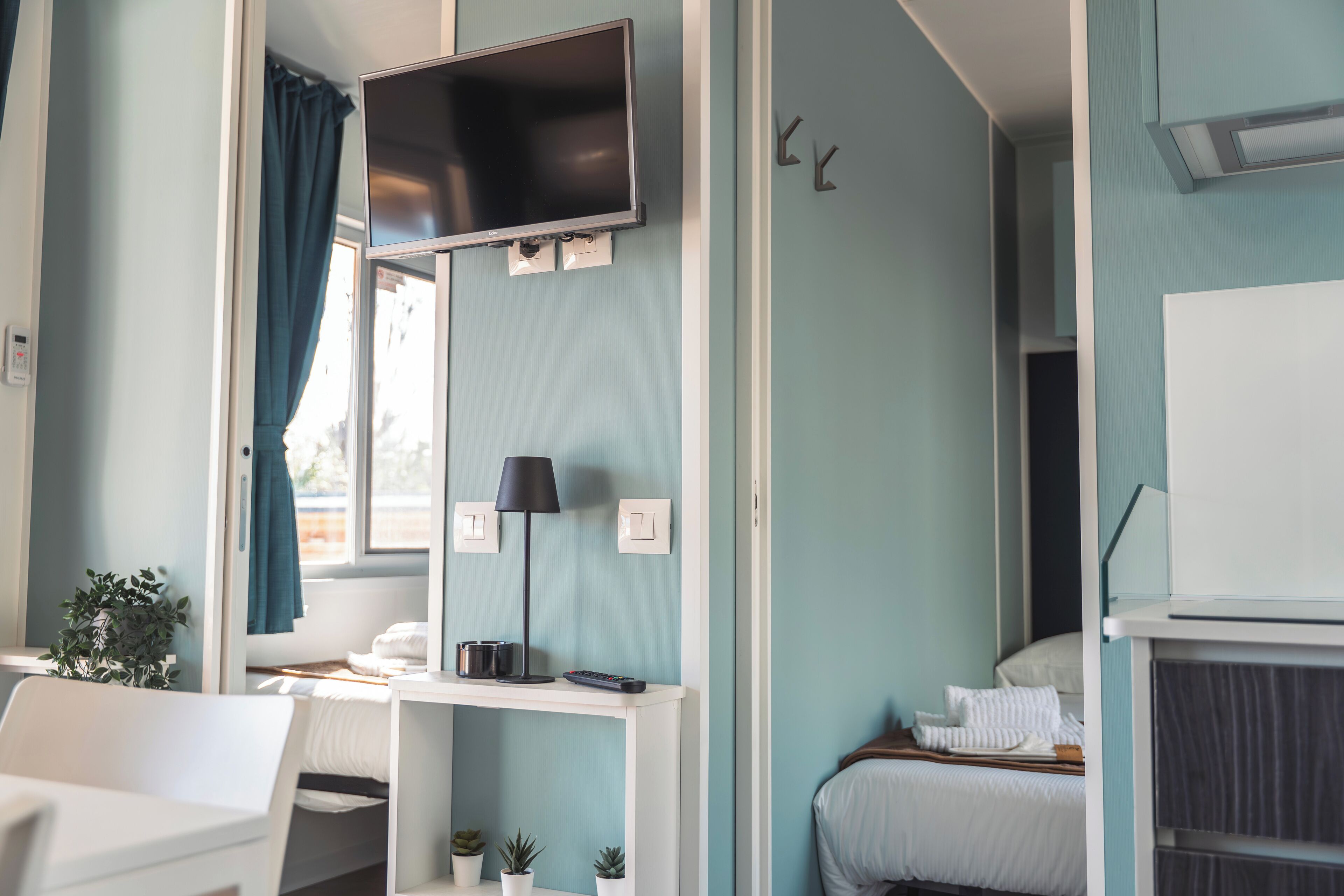A hotel room with a bed, a desk with a lamp, a TV, and a window with curtains.