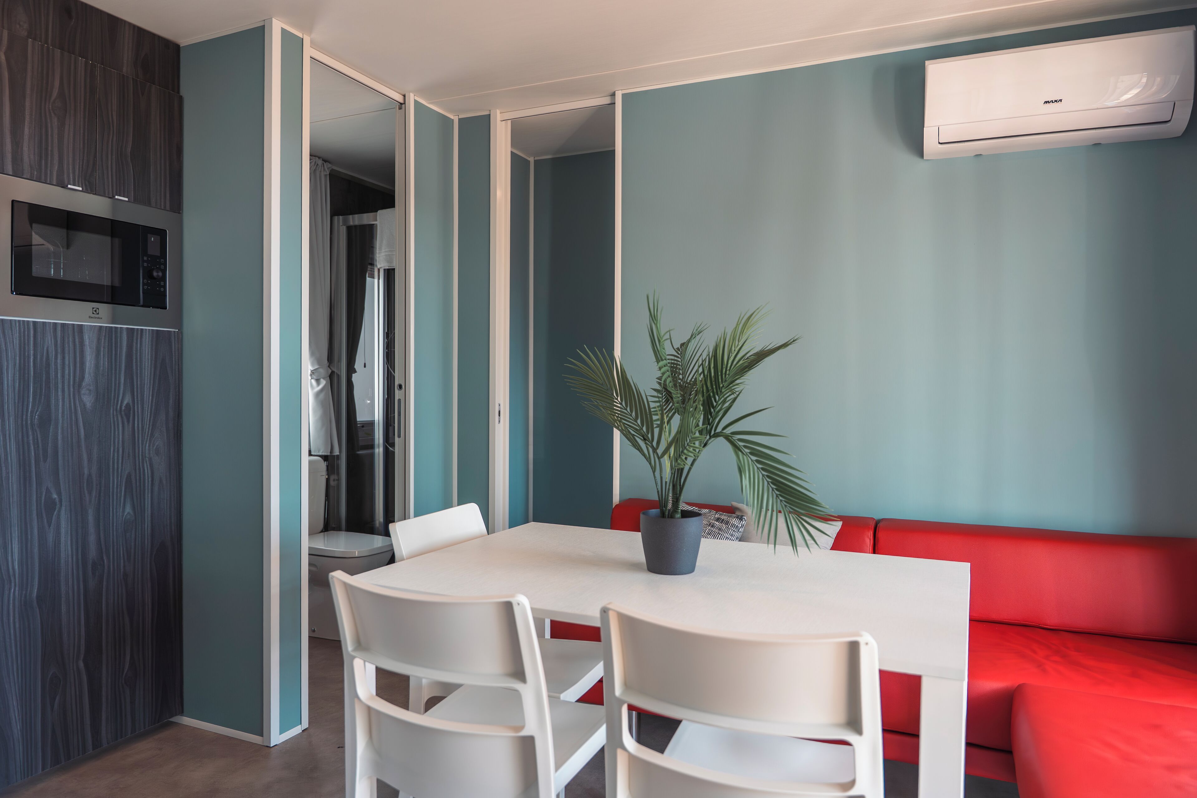 A modern kitchen with a built-in microwave, a dining table with chairs, and a red sofa.