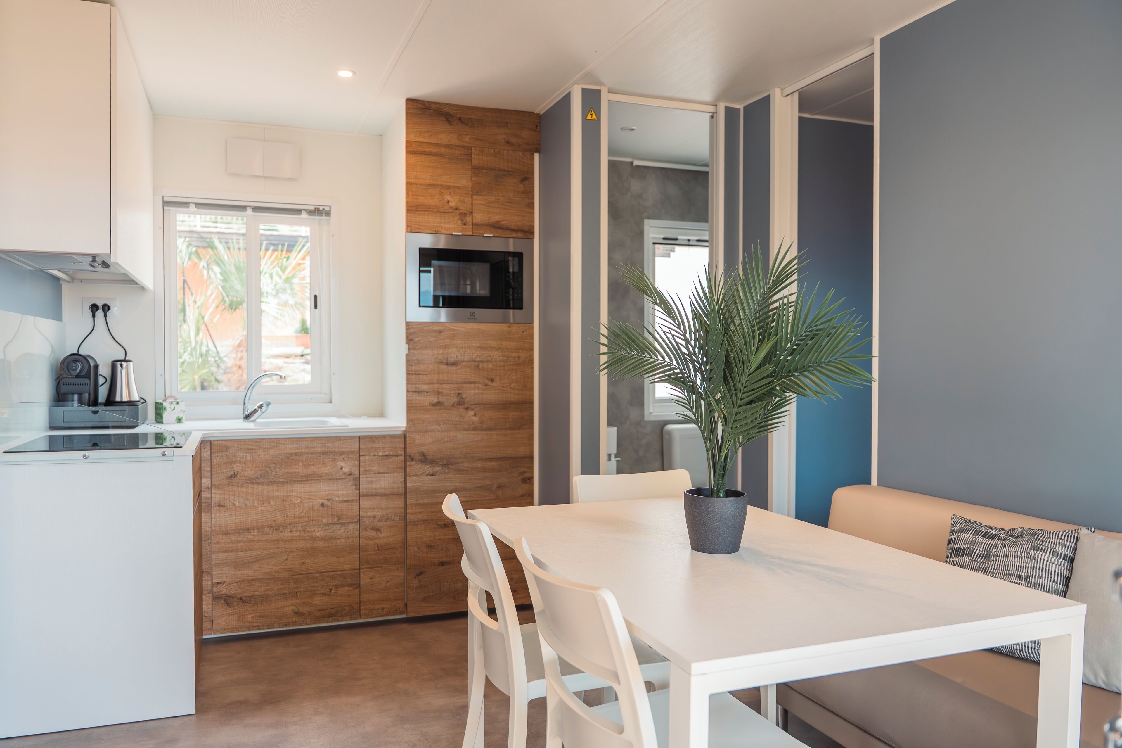 A modern kitchen with wooden cabinetry, a white dining table, and a potted plant.