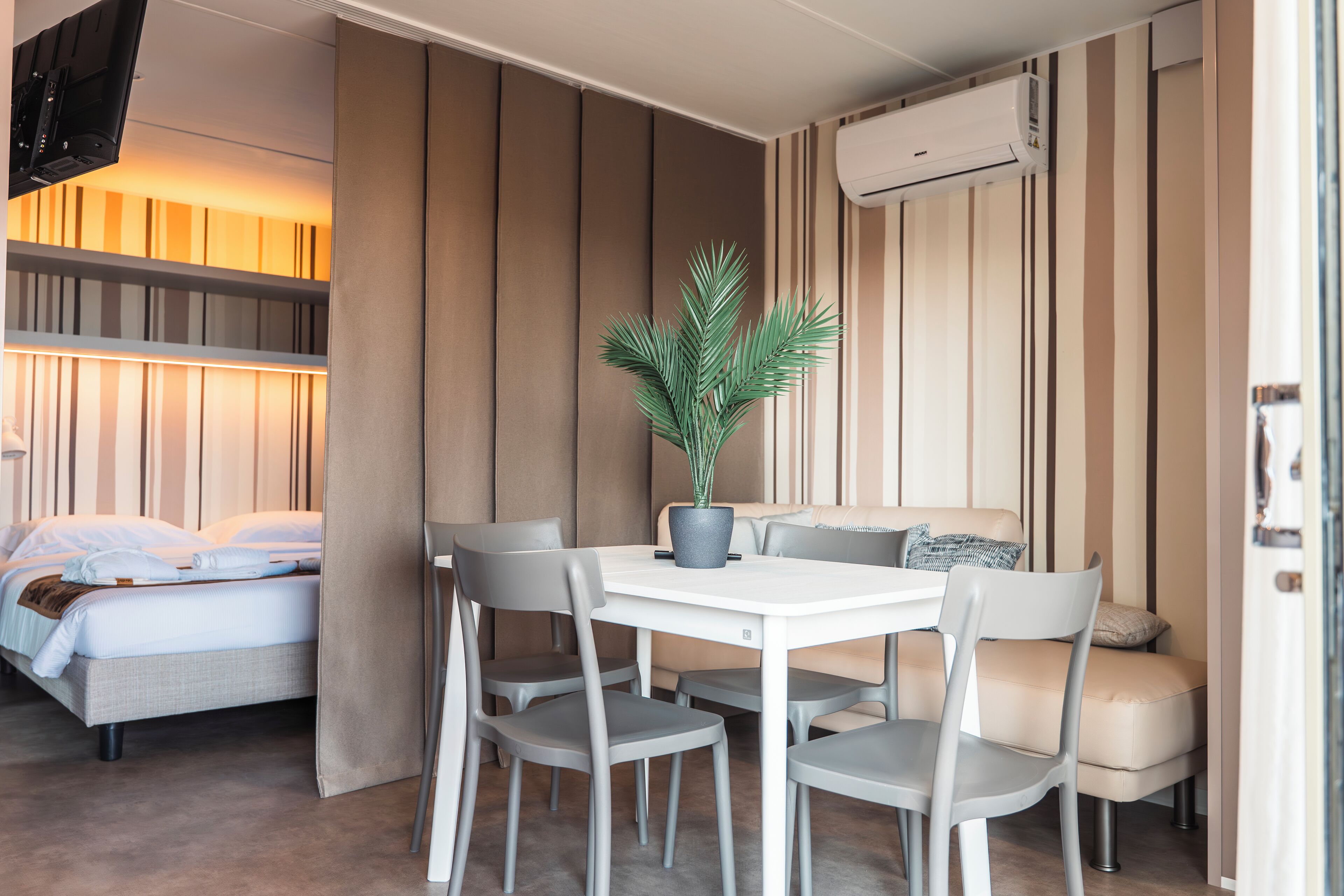A compact room with a bed, a dining table with chairs, a potted plant, and a sofa.