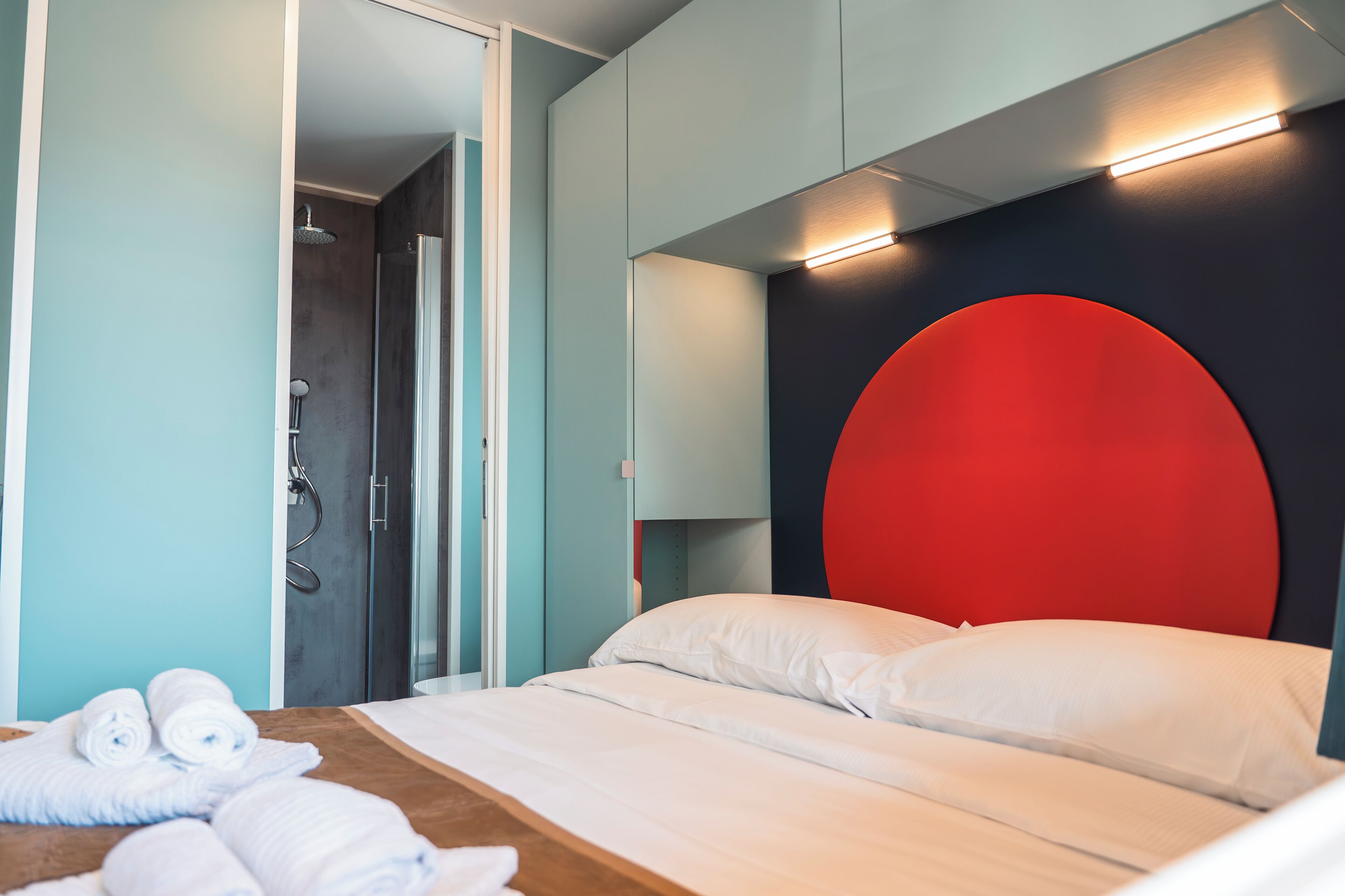 A modern hotel room with a bed, a shower, and a red accent wall.