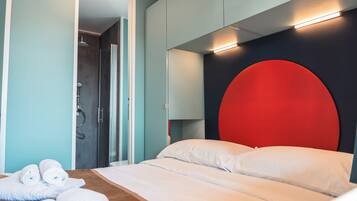 A modern hotel room with a bed, a shower, and a red accent wall.