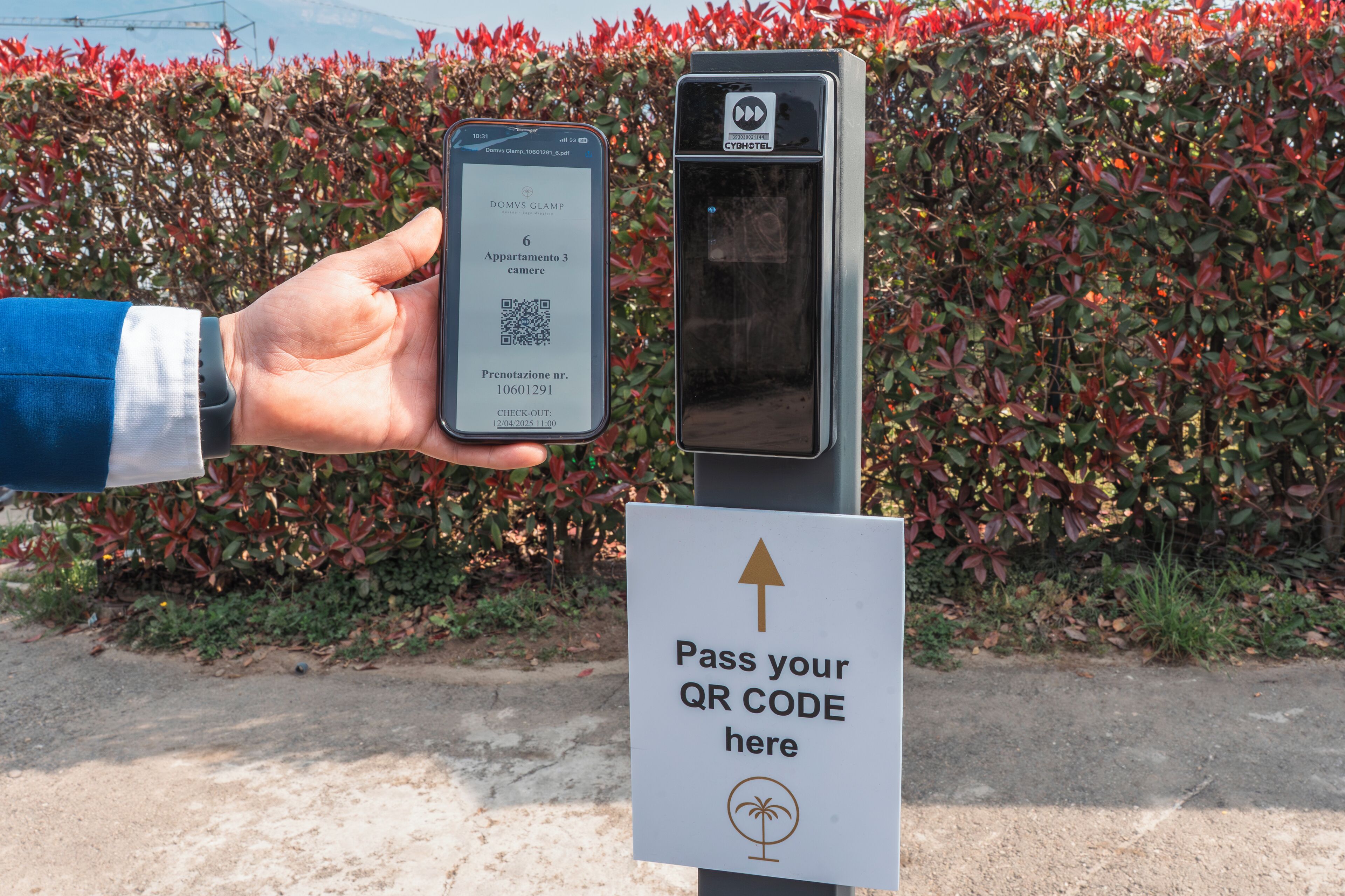 A hand holding a smartphone displaying a QR code, a QR code scanner, and a sign instructing to pass the QR code.