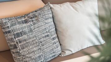 A beige sofa with two pillows, one patterned and one plain, in a room with a light blue wall.