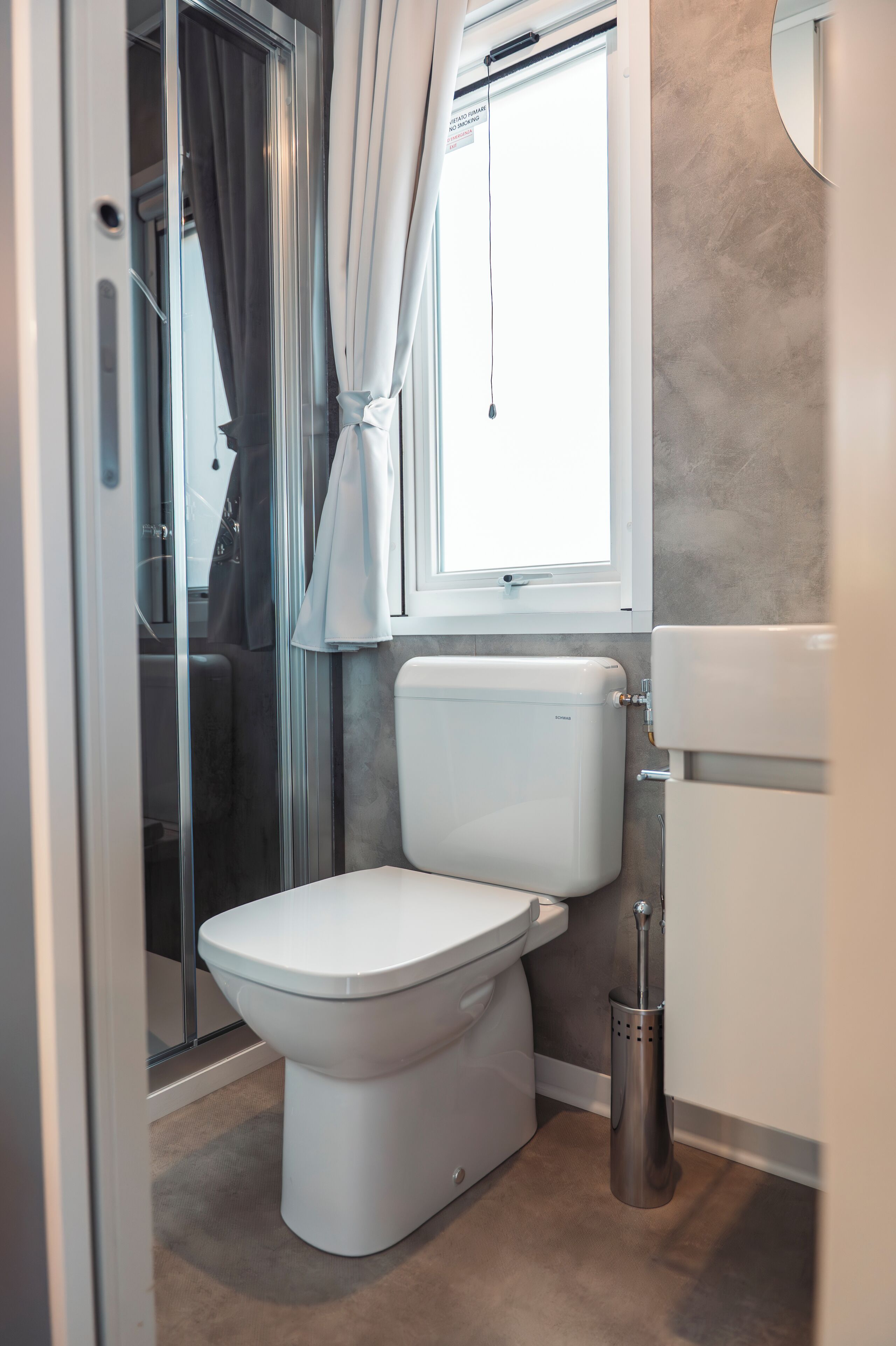 Un baño con inodoro, ducha y ventana con cortinas.